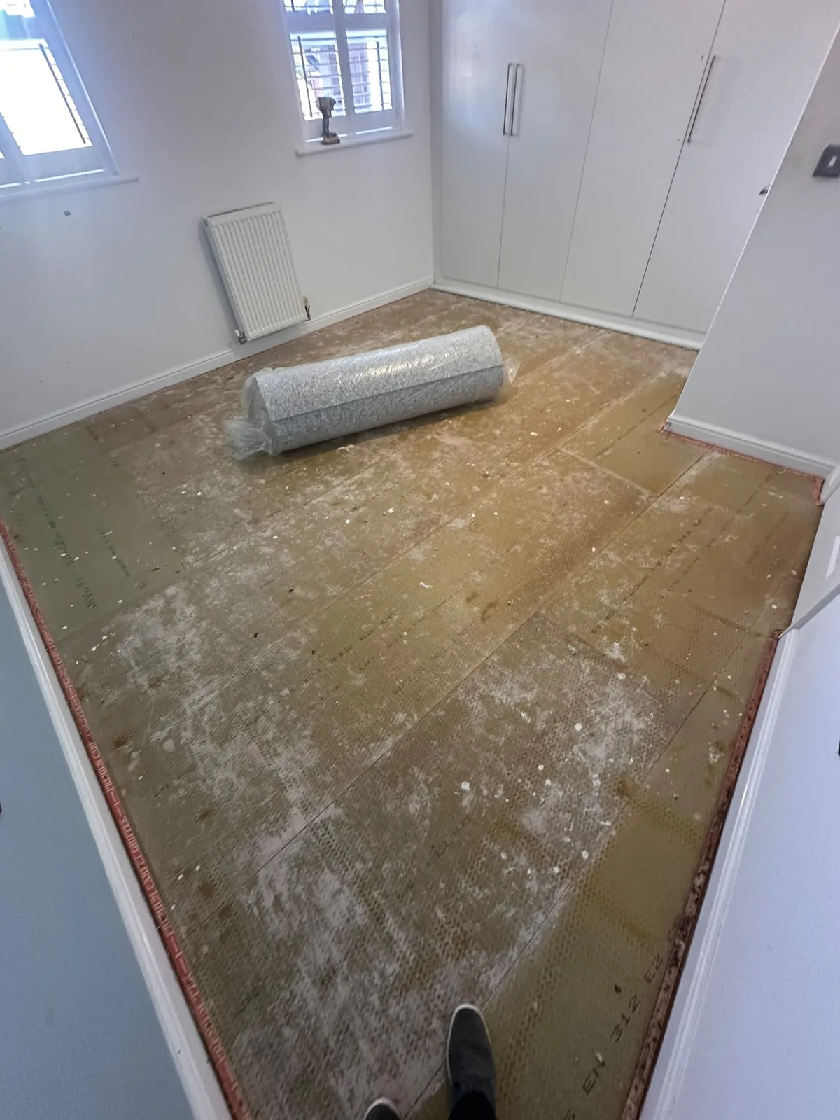 Bare floorboards after uplift with new carpet roll staged for laying — Bromley BR1