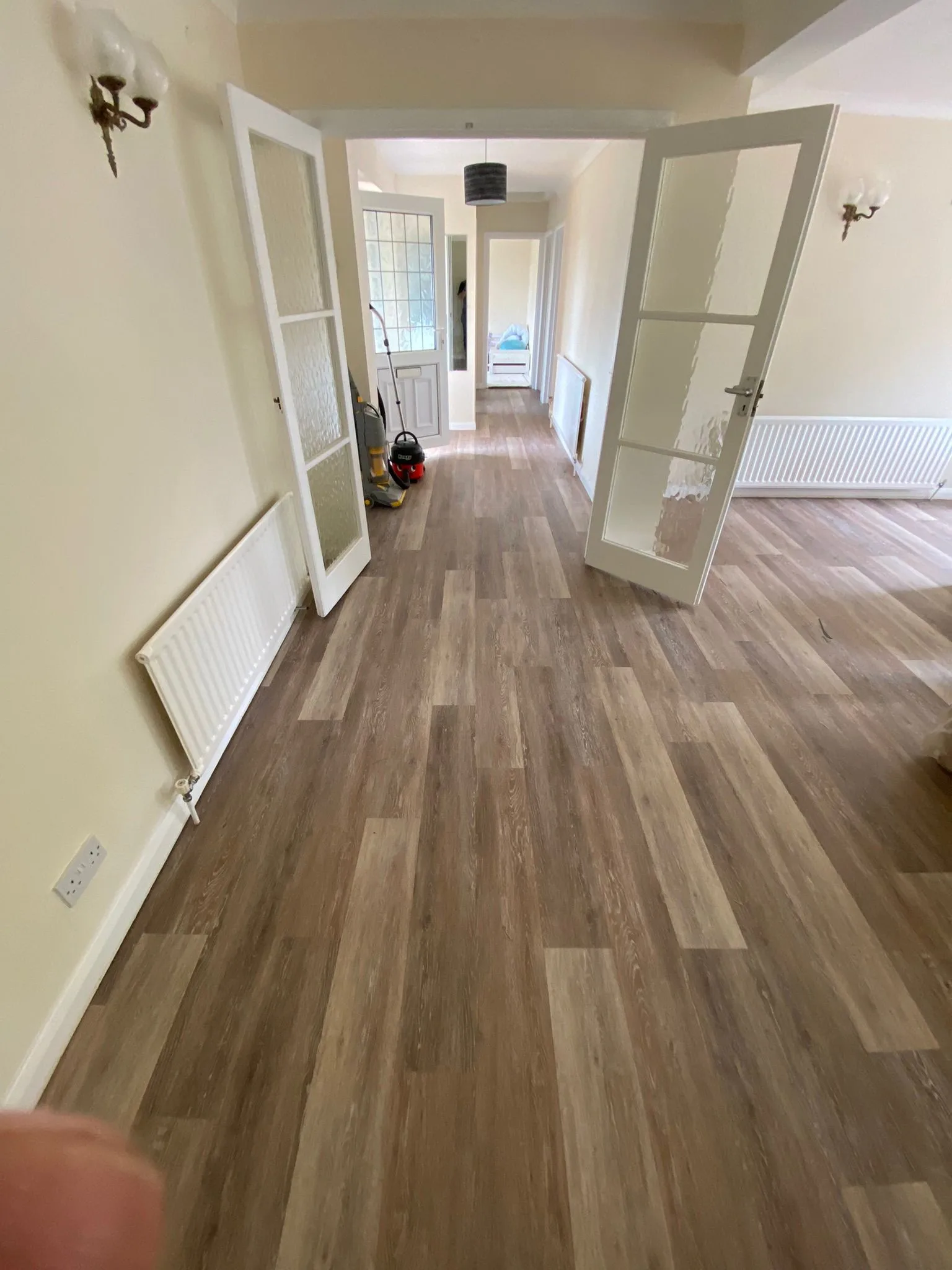 Warm brown wood-effect LVT flooring fitted throughout a wide residential hallway and reception room