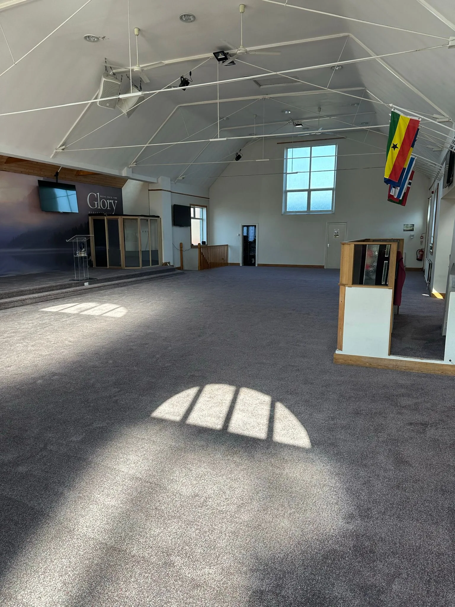 Newly fitted dark grey carpet in a large church hall with natural light casting window shadows across the floor