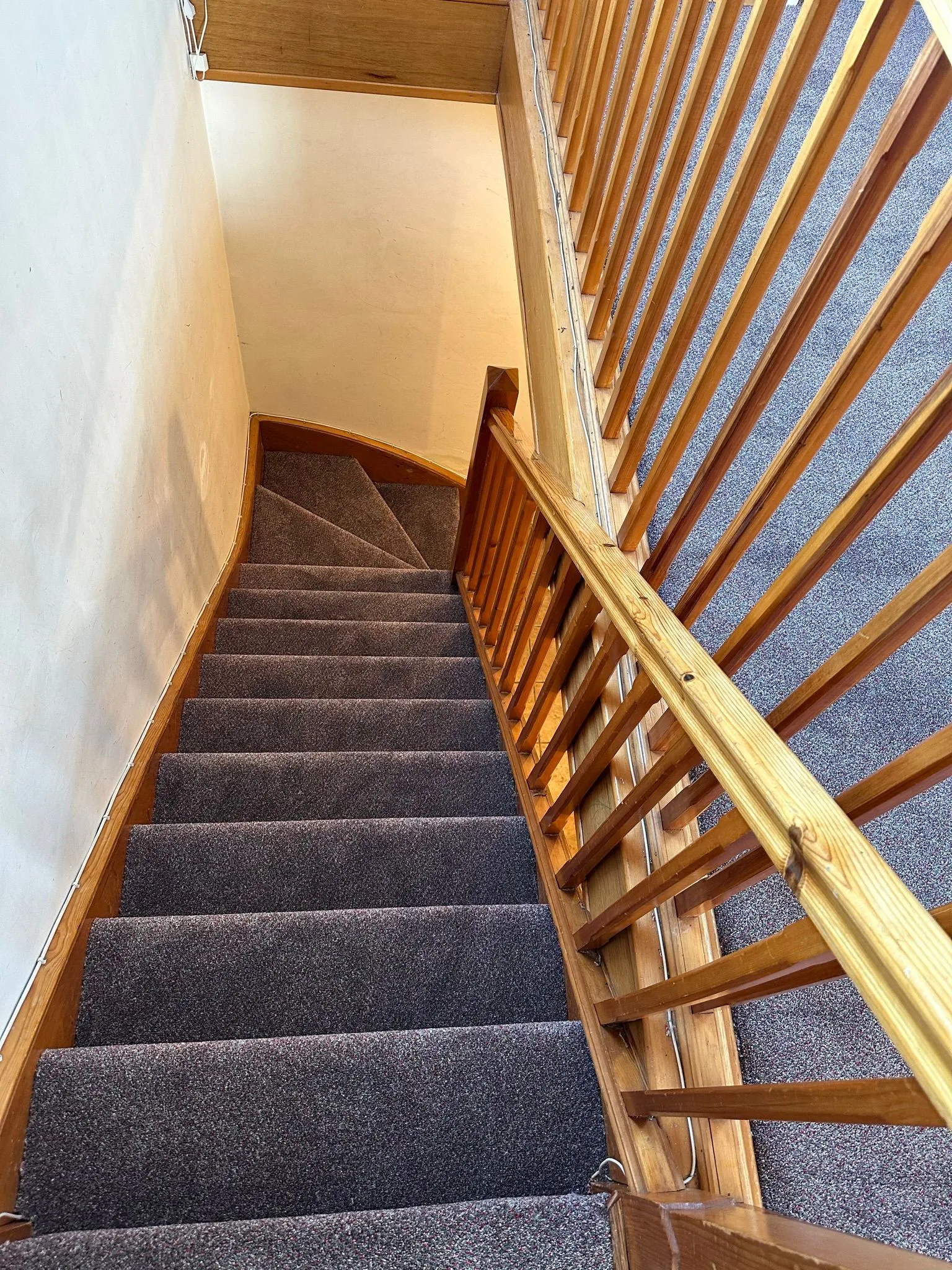 Dark grey carpet professionally fitted on a winding domestic staircase with natural pine wood balustrade