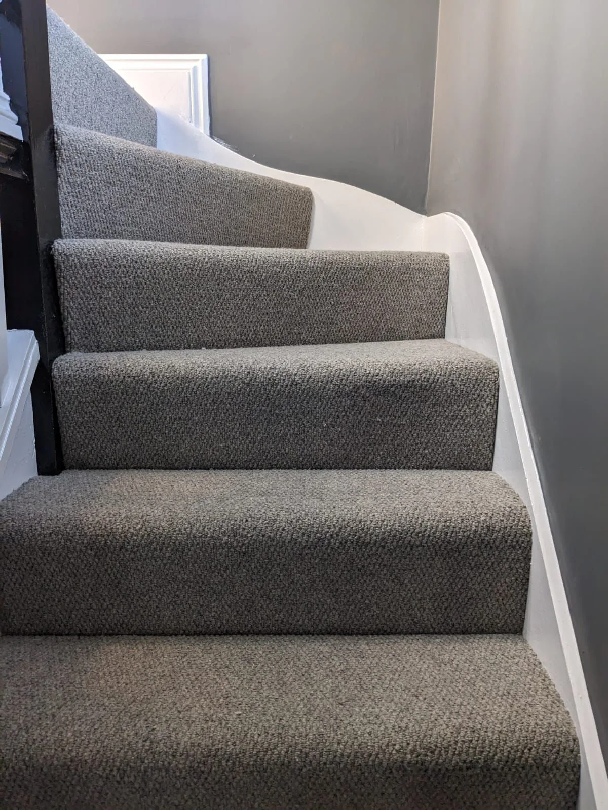 Close-up of grey loop-pile carpet fitted on residential stairs with white painted stringer — detail shot