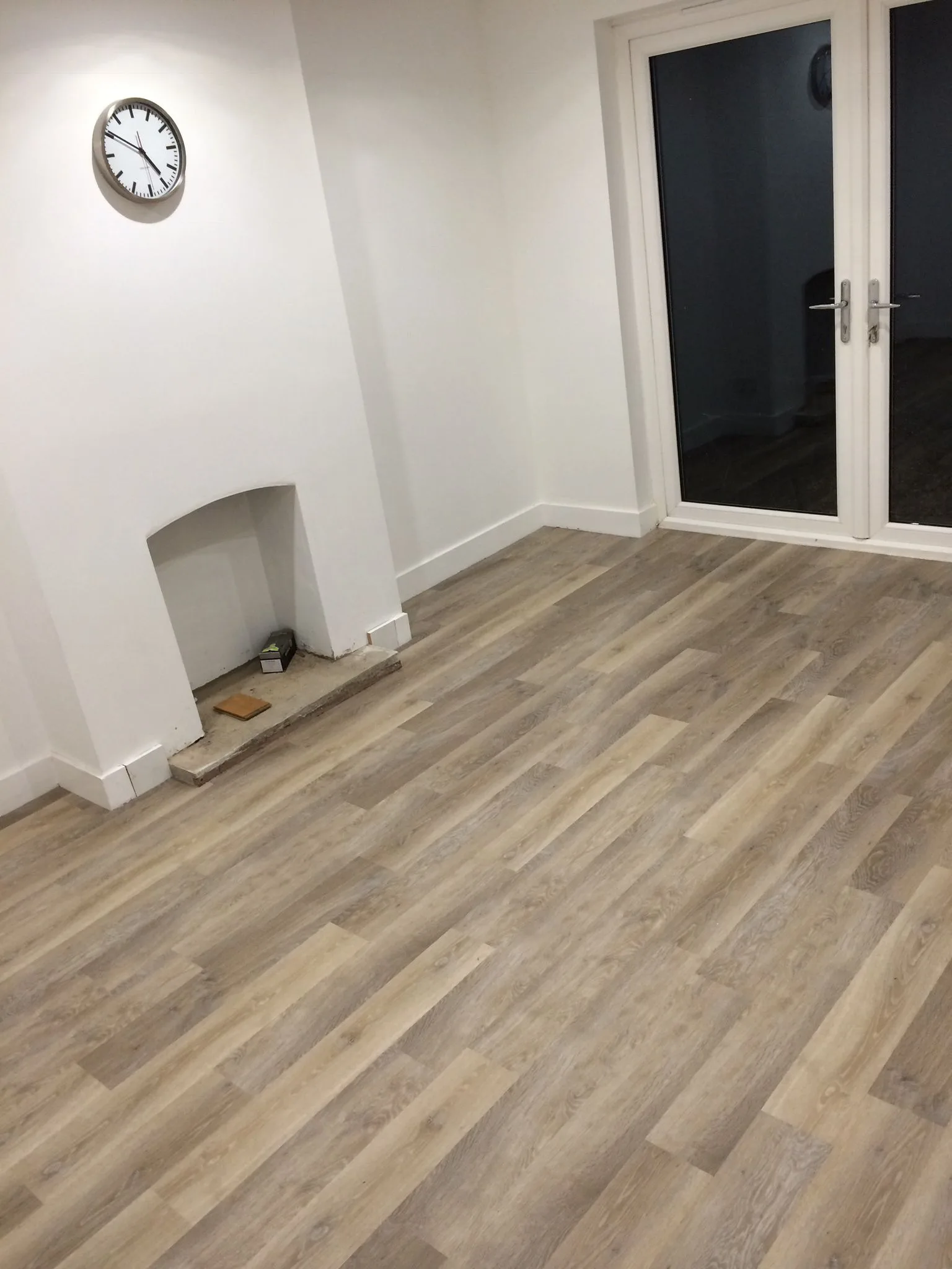 Grey wood-effect LVT flooring fitted in an empty living room with fireplace recess and French doors