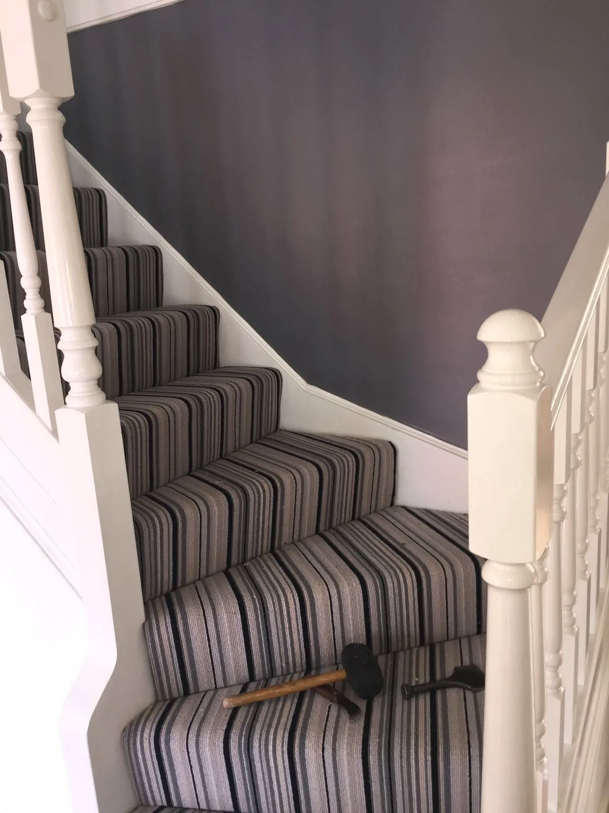 Grey and black striped stair carpet fitted on a Victorian staircase with white balustrade and dark grey feature wall