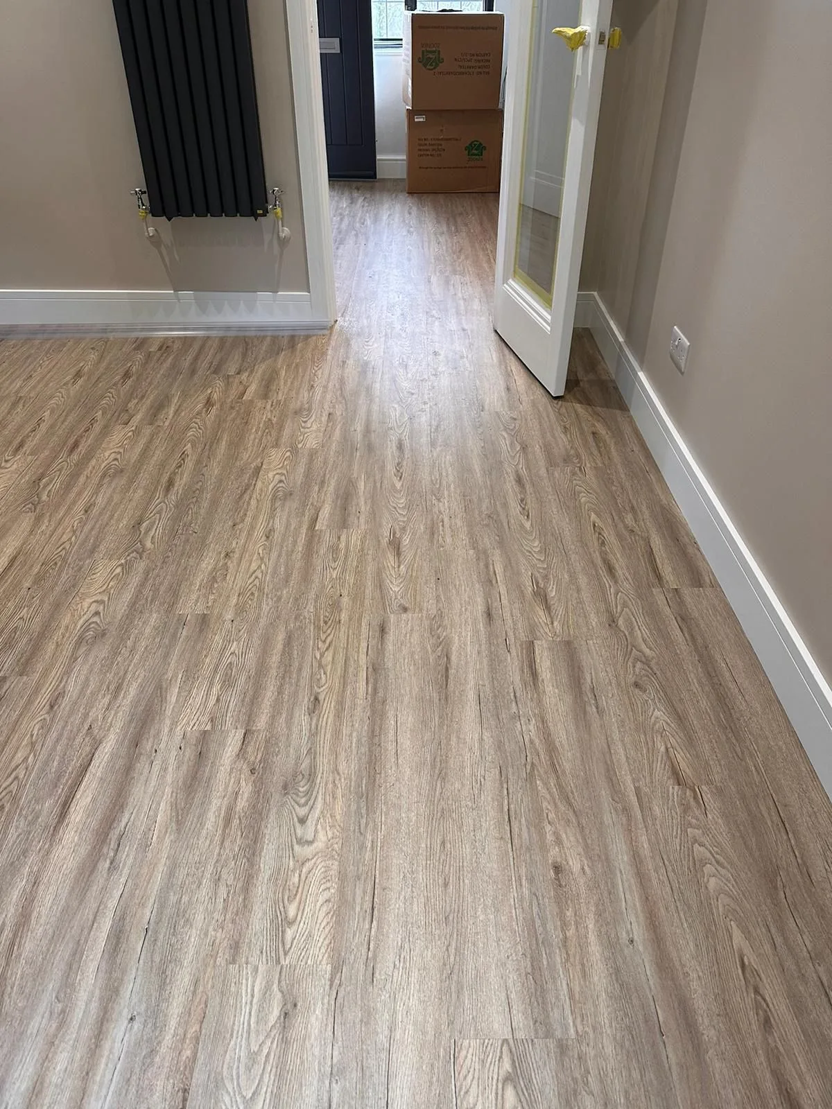 Natural oak wood-effect LVT flooring fitted in a residential hallway with vertical designer radiator